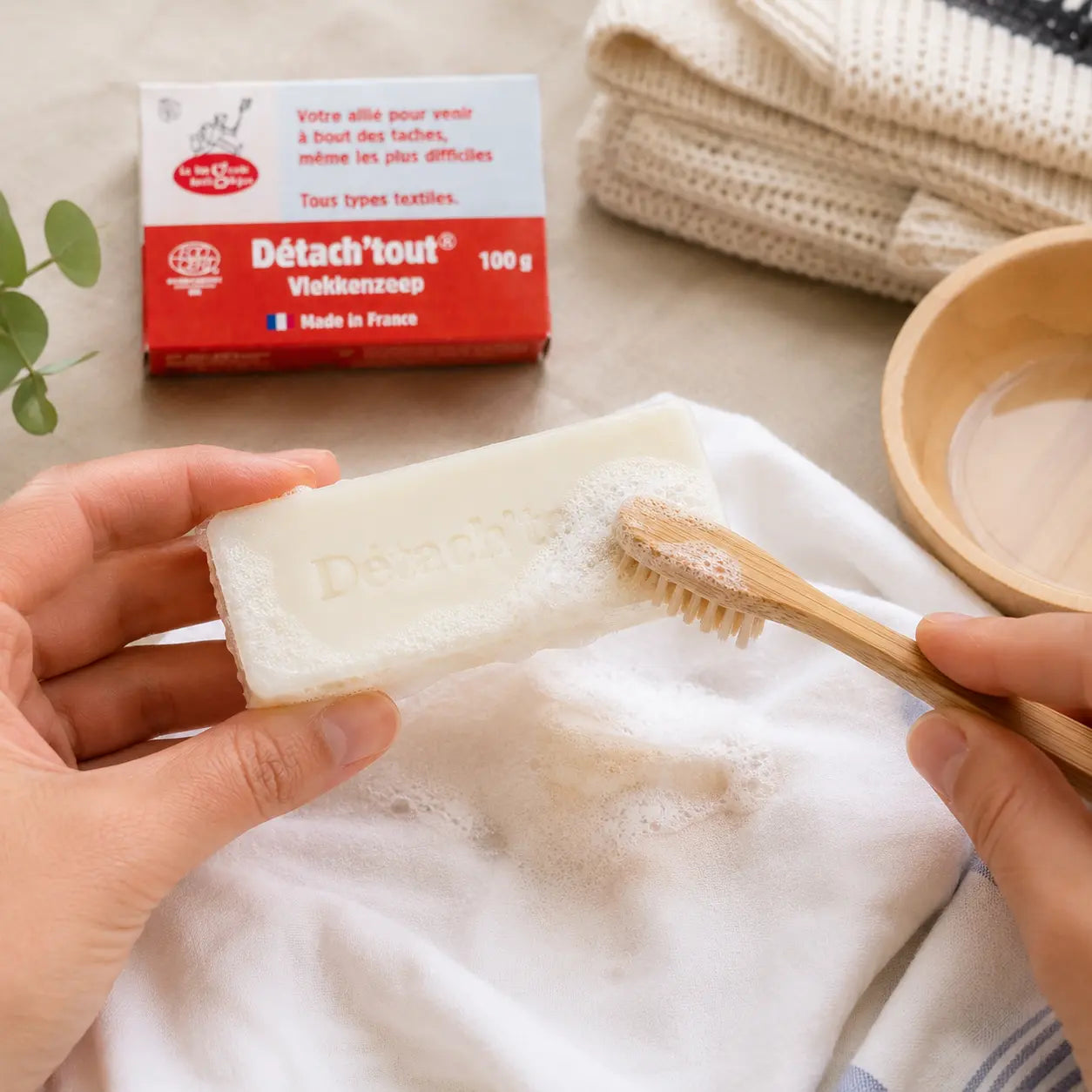 Jabón quitamanchas ecológico creando espuma con un cepillo de bambú sobre tejido blanco en un entorno zero waste.