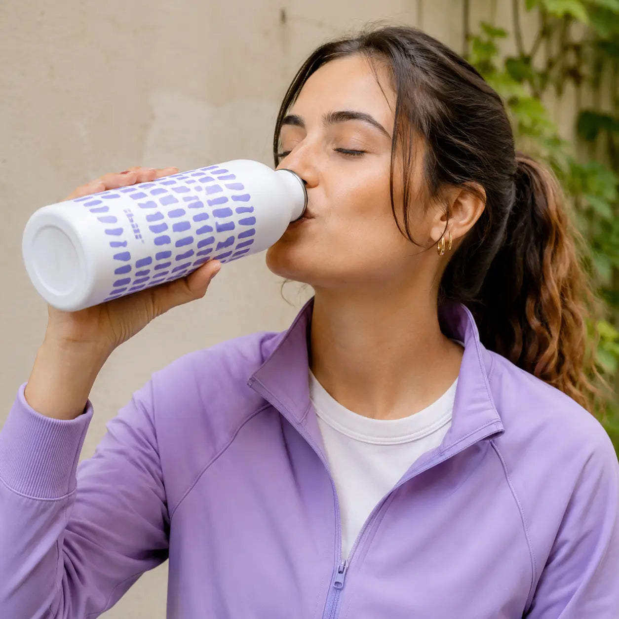 Mujer bebiendo de una botella térmica reutilizable de acero inoxidable IBILI de 500 ml color blanco y lila